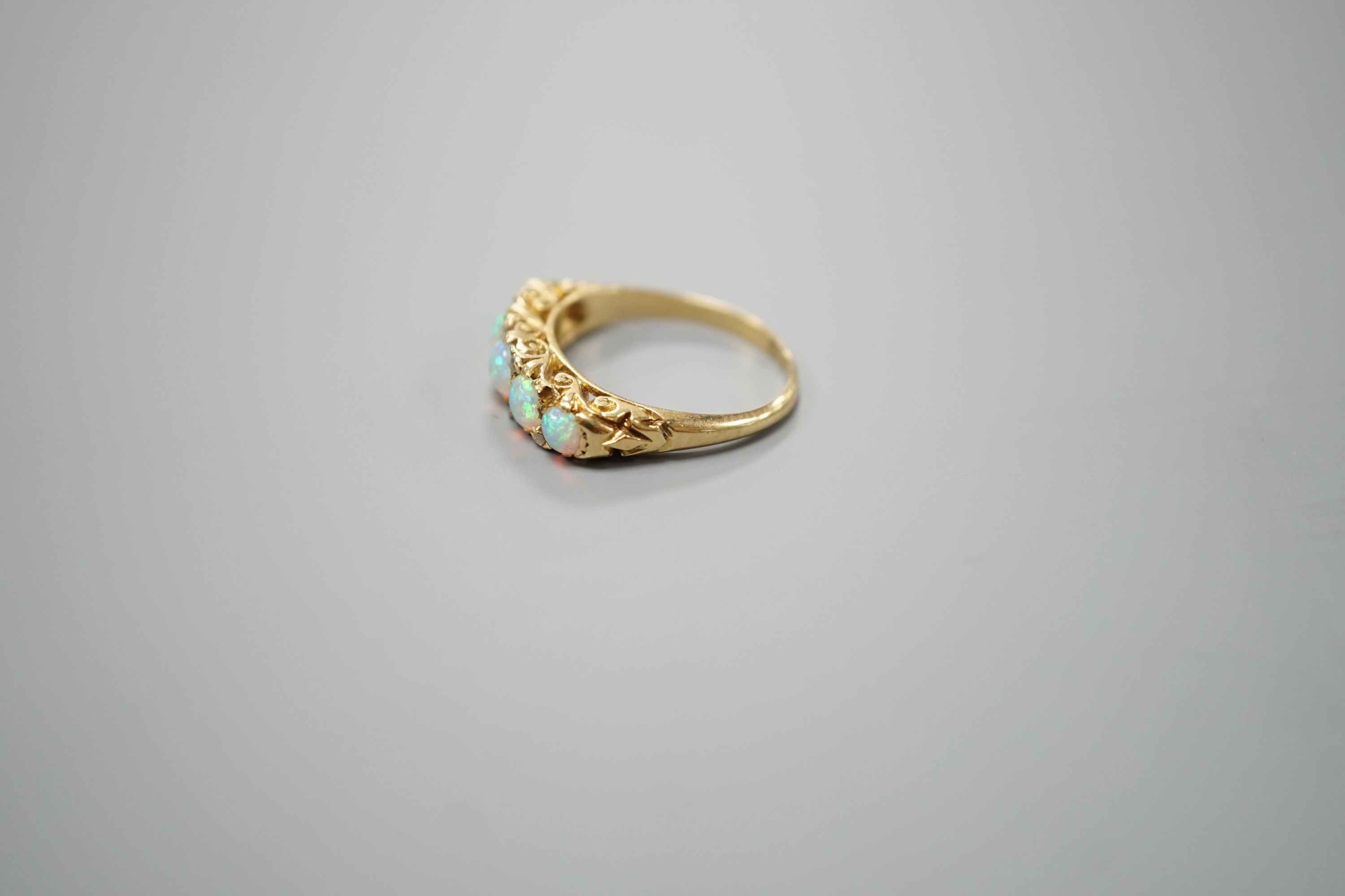 A late Victorian yellow metal and graduated five stone white opal set half hoop ring, with diamond chip spacers, size M, gross weight 3.7 grams.